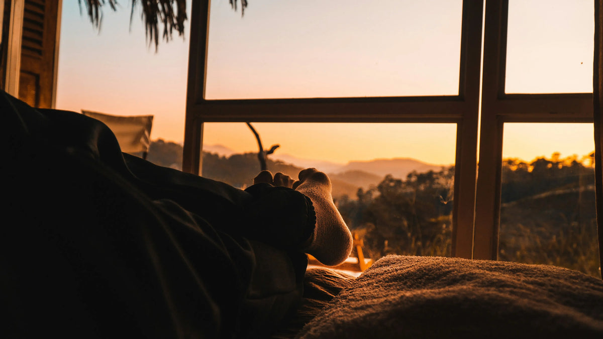 Sock-covered feet on a bed beside a window in warm evening light